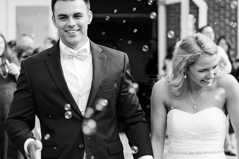 Wedding Photographer, Bride and Groom walk smiling amidst bubbles