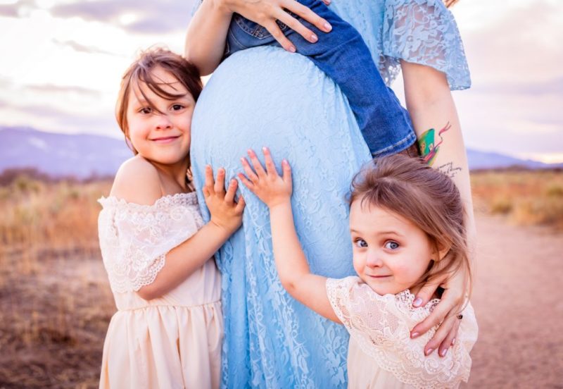 close up maternity picture with children and tatoo of angel baby with mountains in the background schedule maternity pictures at 27 weeks